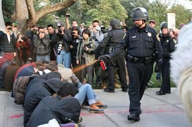 Police officer sprays a group of sitting students